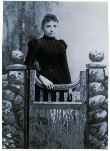 Black and white photo of woman standing next to a gate.