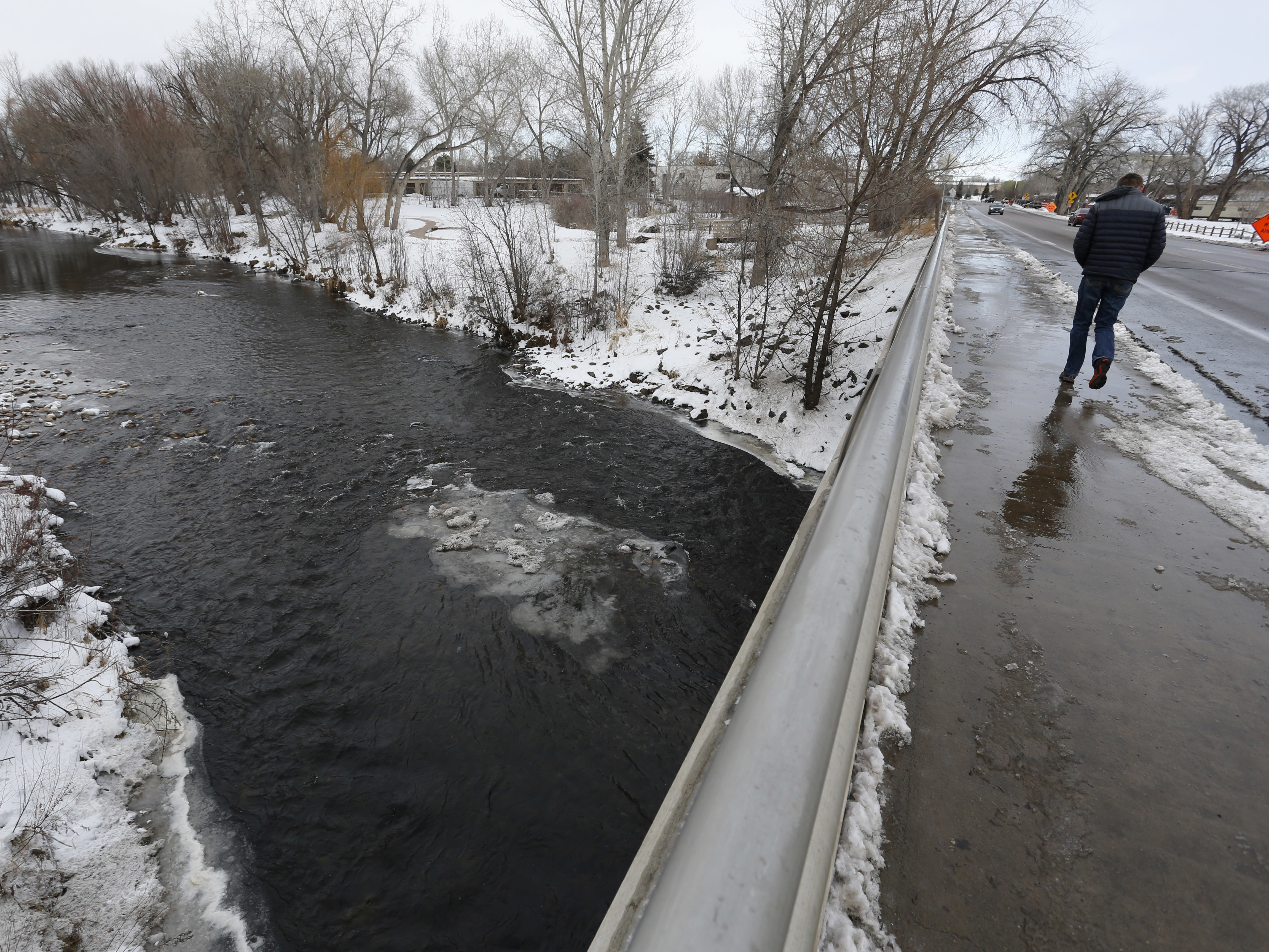 A man crosses a bridge over the Poudre River, in Fort Collins, Colo.