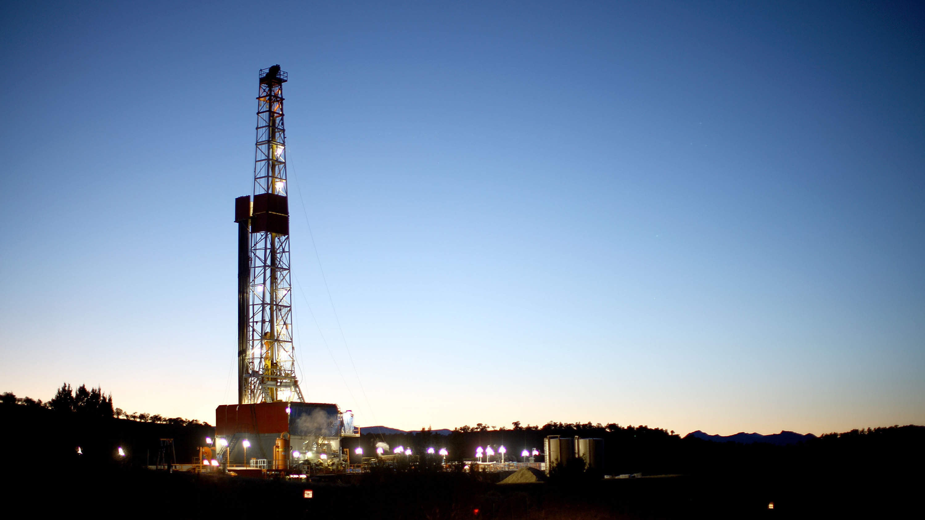 A natural gas drilling rig's lights shimmer in the evening light near Silt, Colo.