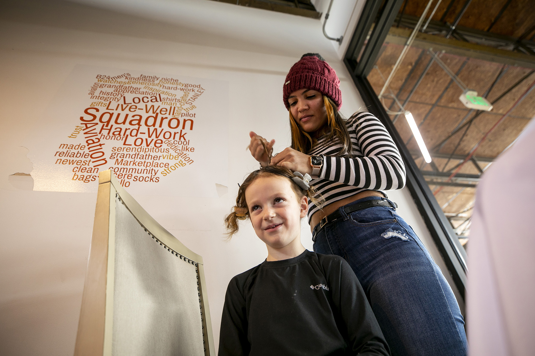 Janecy Rodriguez braids hair for Layla (5) as she and other asylum seekers run stalls to sell goods and make some money in an otherwise empty suite at Stanley Marketplace. Jan. 16, 2024.