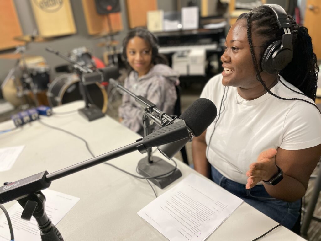 Two teenagers sit at microphones in a recording studio to record the podcast, "Youth on Rewind"