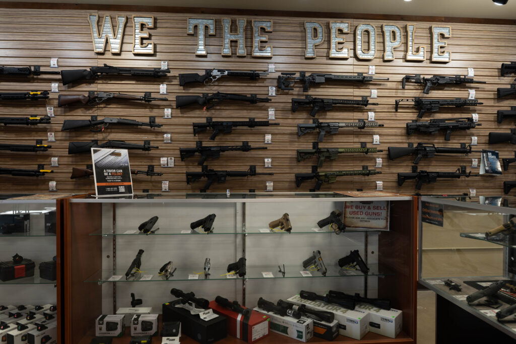 A wall display of long guns and a display case of pistols under a display that reads "We the People" in a Jefferson County gun store.
