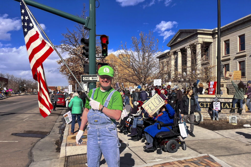 Man in costume waves flag with group of people behind him.
