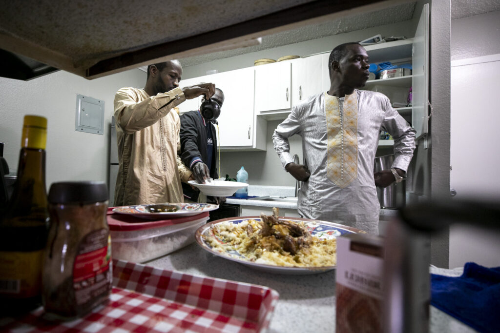Three men stand in a kitchen after lunch and tea before Friday prayer