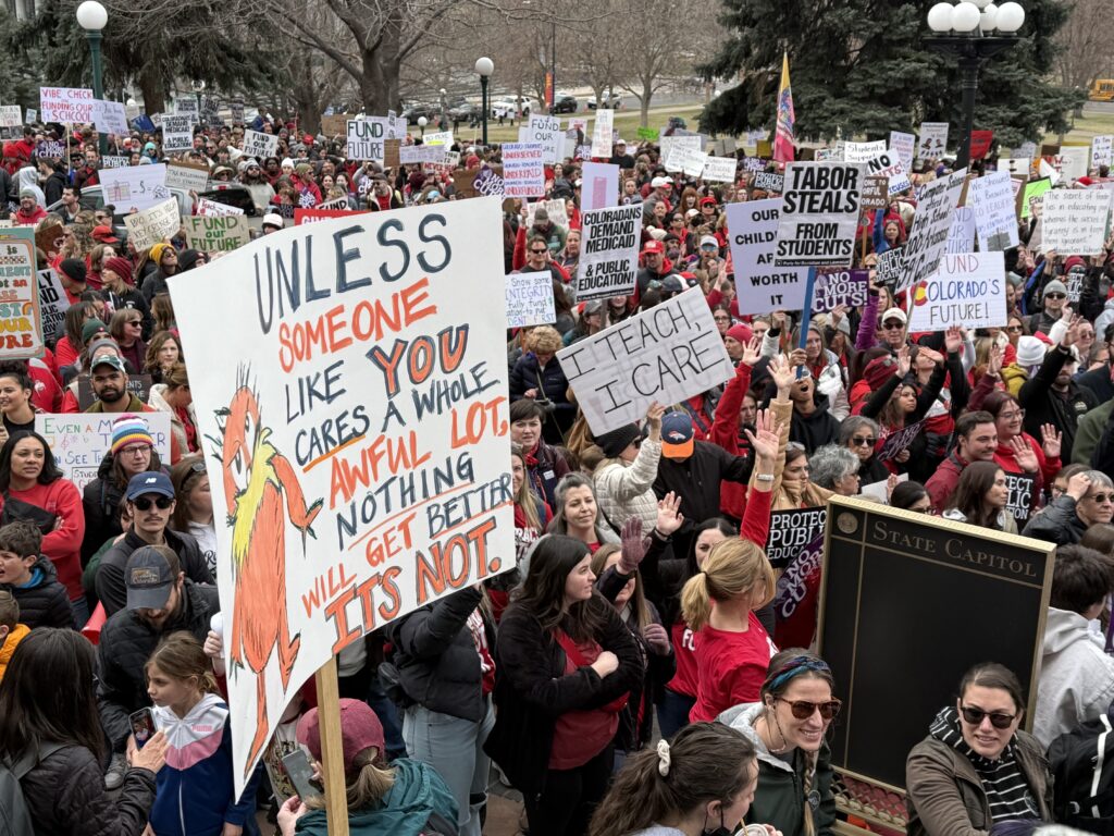 A massive crowd gathers holding up signs like "I teach, I care" and "TABOR steals from students"