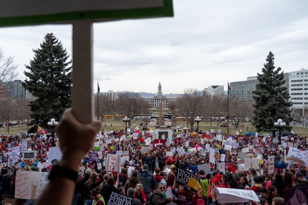 A long view of the City and County Building in downtown Denver with a masive crowd of protesters in the foreground.