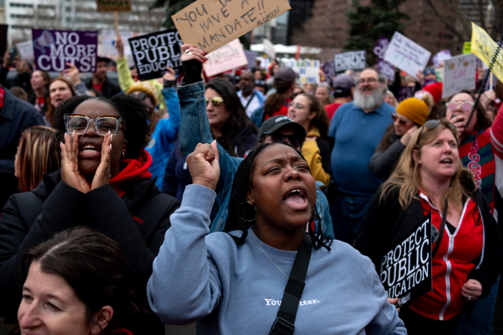 In the foreground two women yell in the crowd of protesters, background.