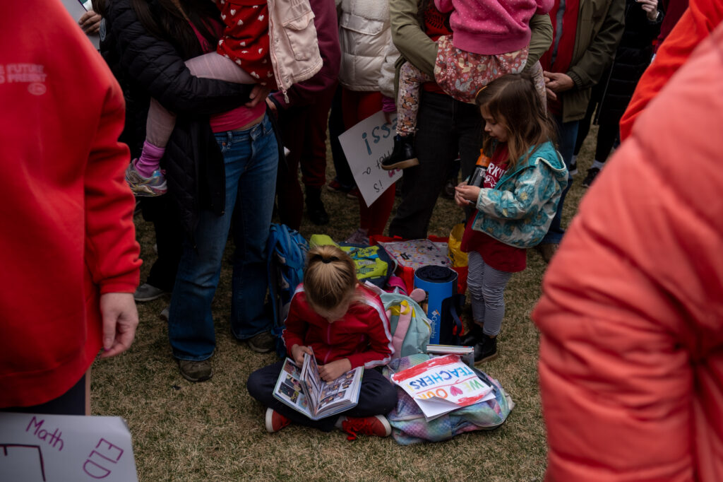 Two young girls sit in the standing crowd of protesters.