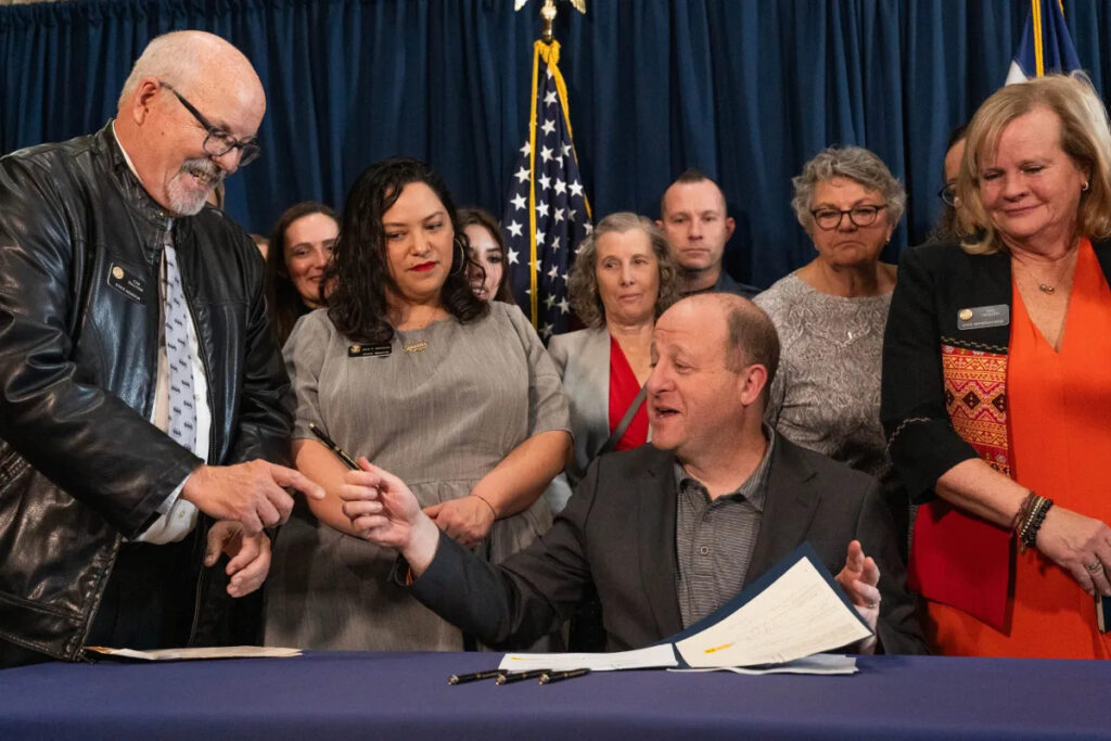 Colorado Gov. Jared Polis, center, hands a pen he used to sign Senate Bill 3 into law