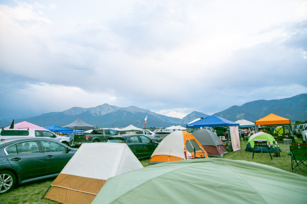 A field full of tents and cars sit up against a wall of tall peaks.