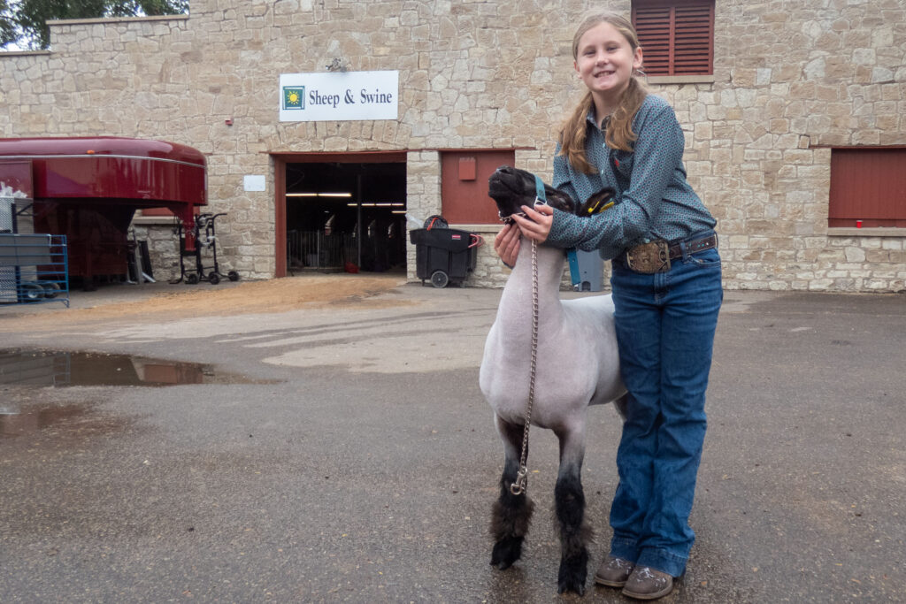 a child with long hair holds a lamb in front of a stone building