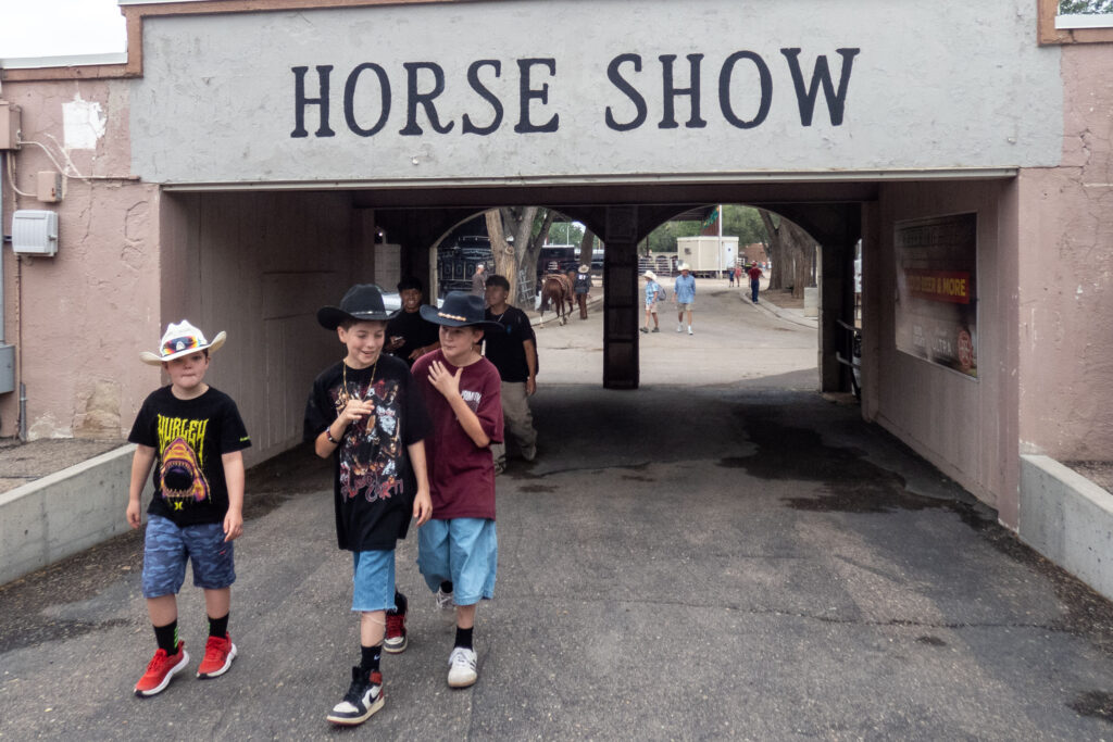 three young people dressed in shorts, t shirts and cowboy hats walk through an archway that says horse show