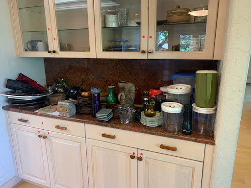 Photo shows kitchen cabinets with dishes and other kitchen items stacked on the countertop.