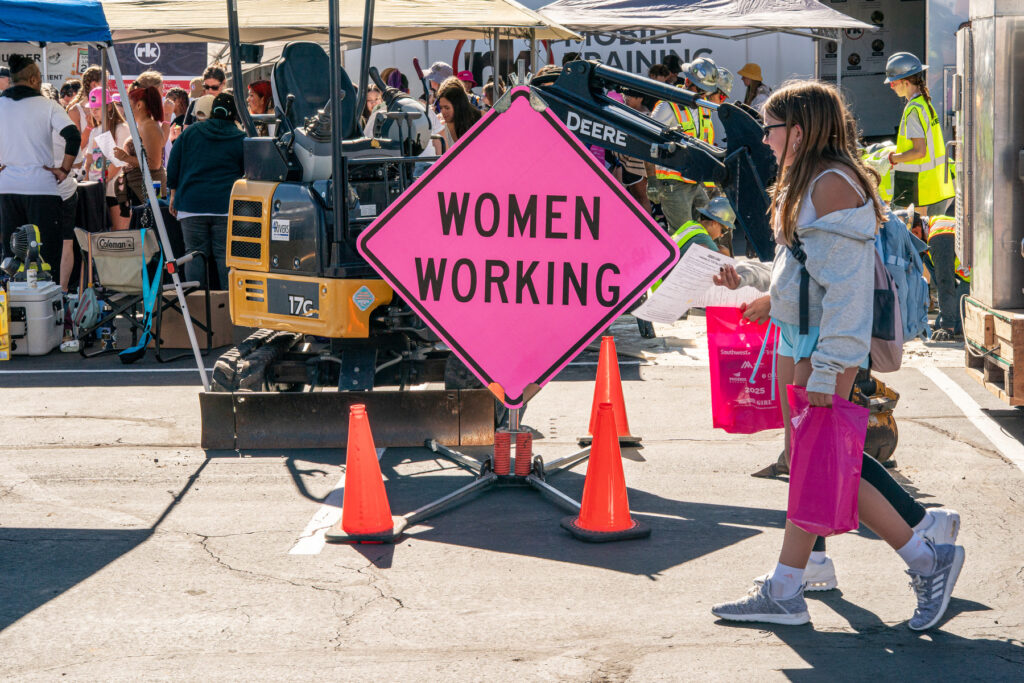Girls walk past a pink Women Working sign