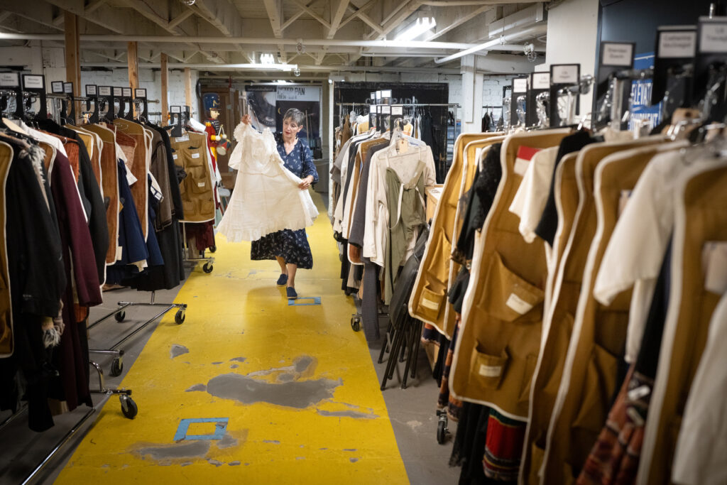 A woman holds up and carries a white dress to be worn by a character in Dracula