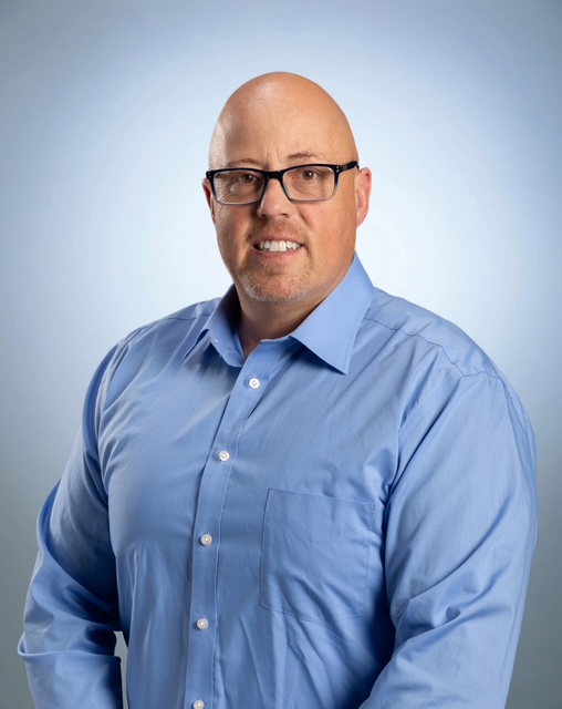 a head and shoulders portrait of a person wearing glasses and a blue button shirt