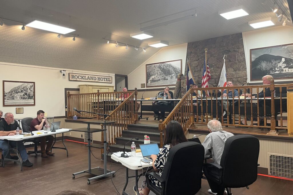 a wide shot of several people at two tables facing toward a raised area with the commissioners at a long table