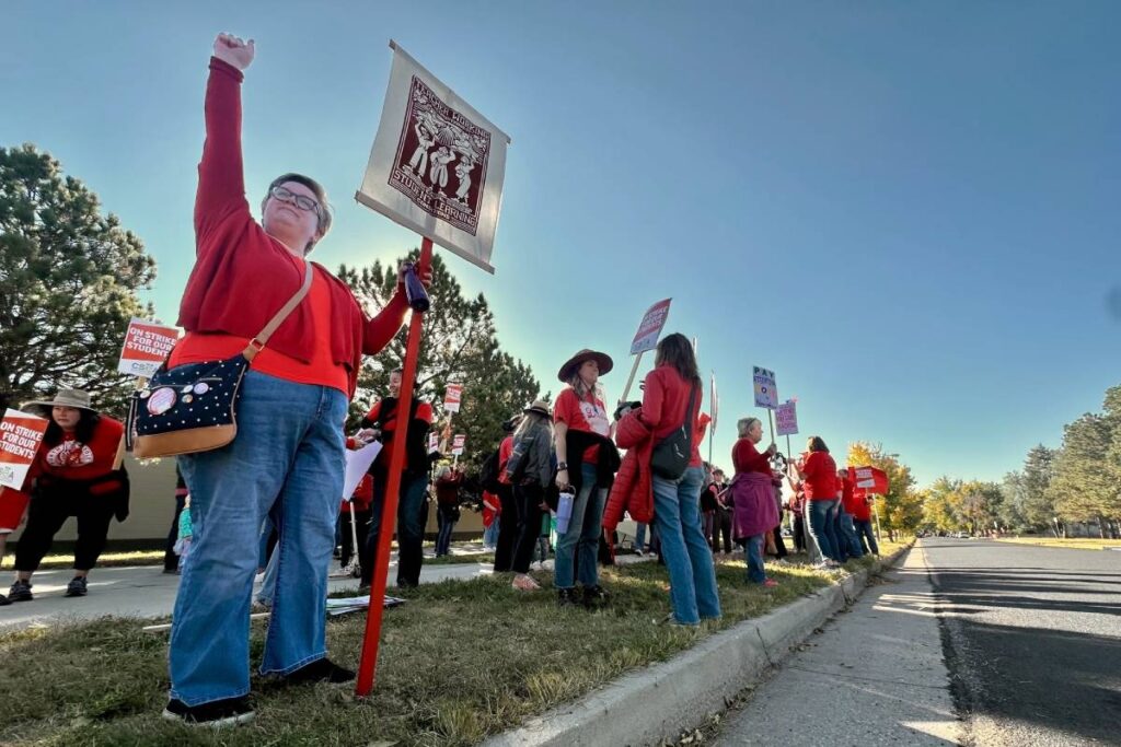 A woman wearing red raises her fist while holding a sign along with other striking teachers