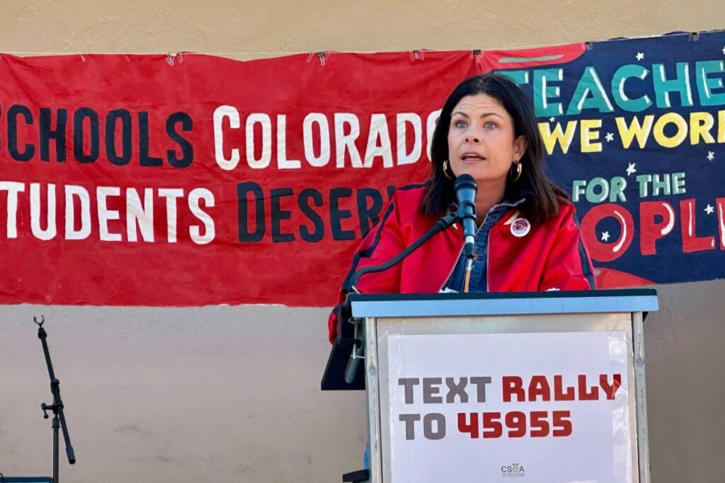 A woman speaks from a podium at a rally for teachers.