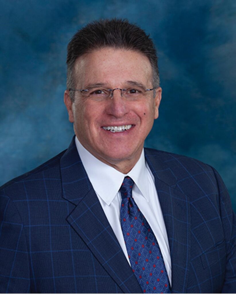 A man wearing a blue suit and tie is smiling for the camera.