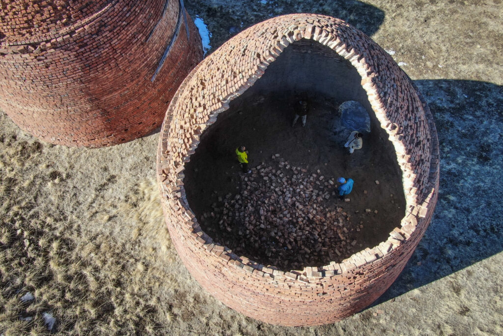 four people standing in a large, open domed brick structure a portion of another similar structure stands nearby