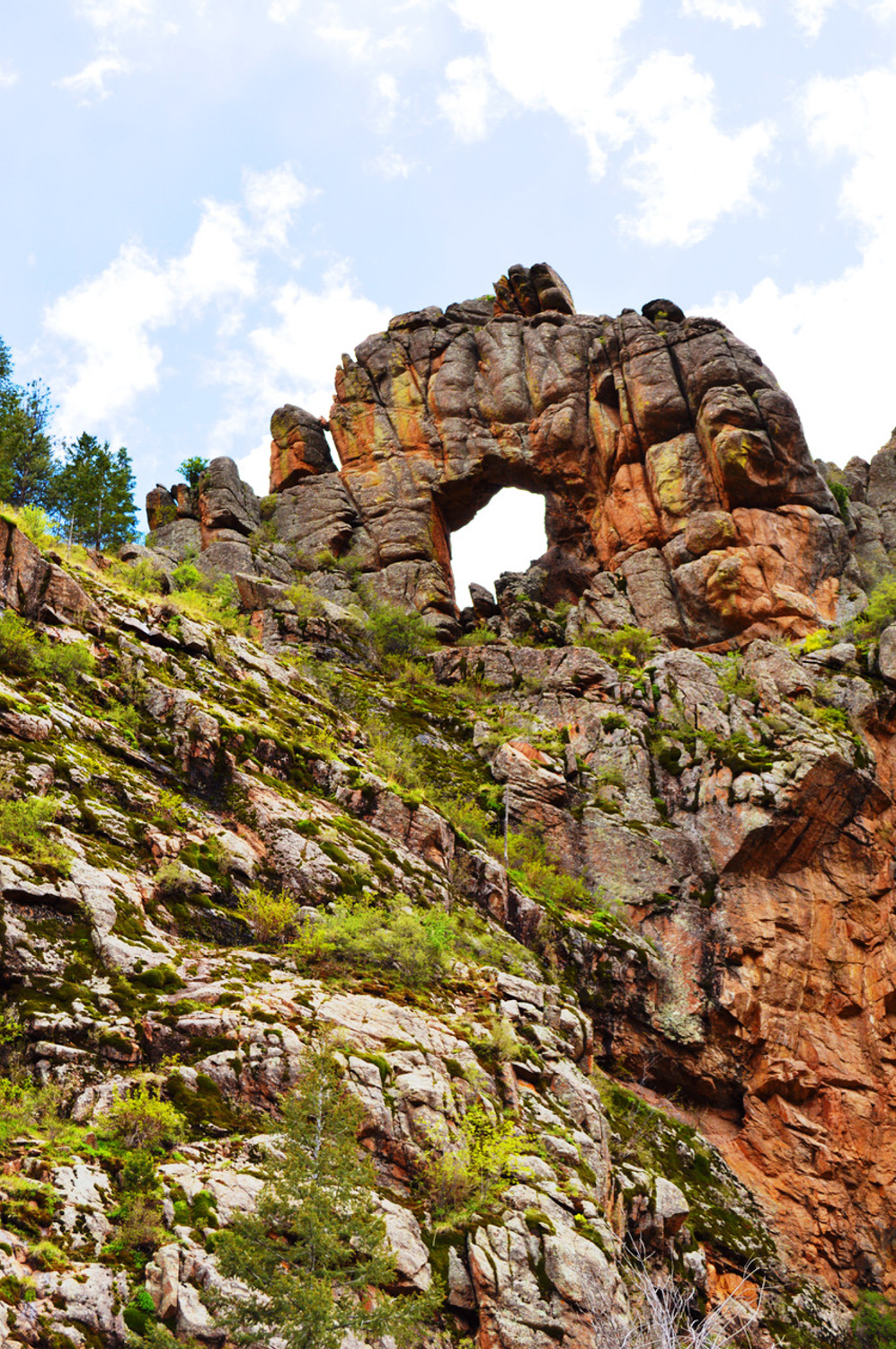 natural arched rock formation with a large hole in the middle situated on a steep hillside