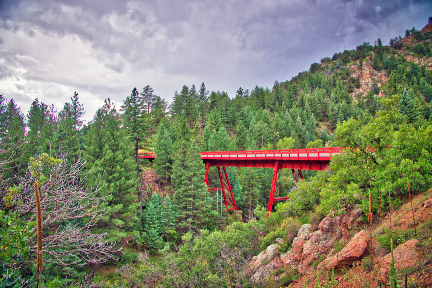 a red bridge crossing over a small gorge, surrounded by trees